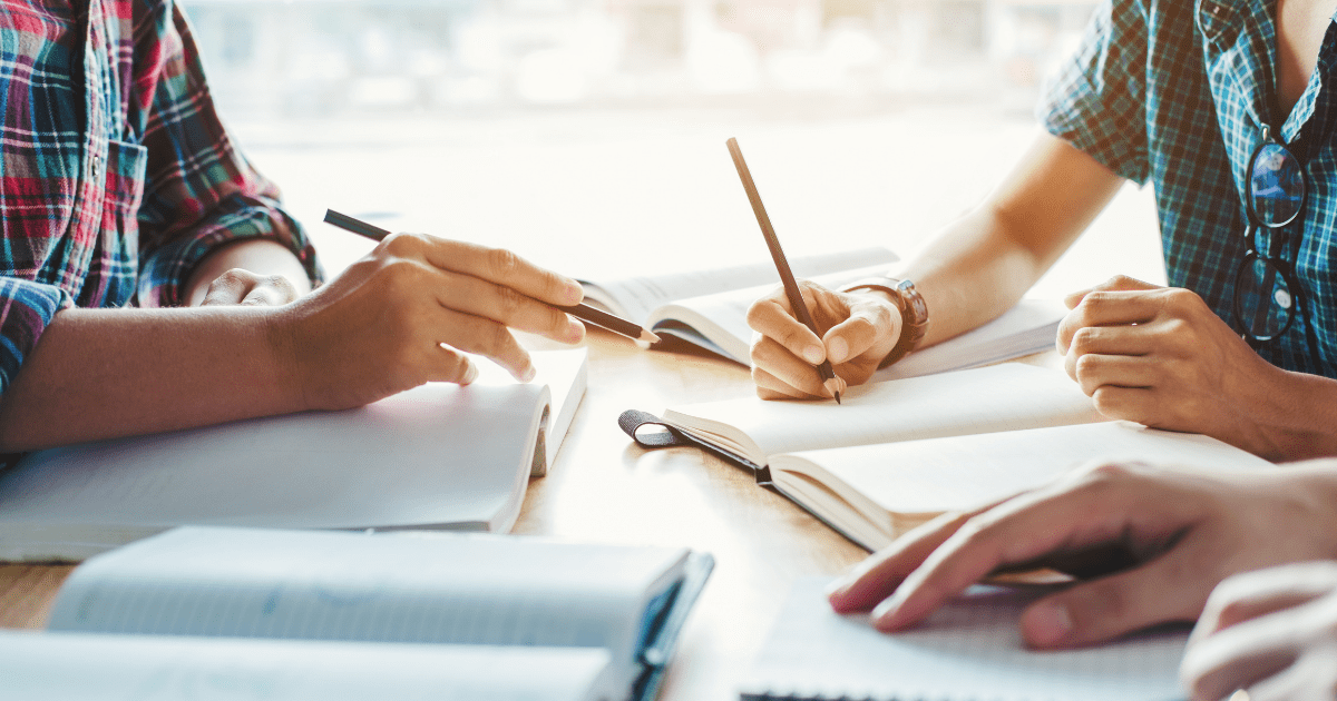 Student: Three students sit around a desk writing with pens on paper