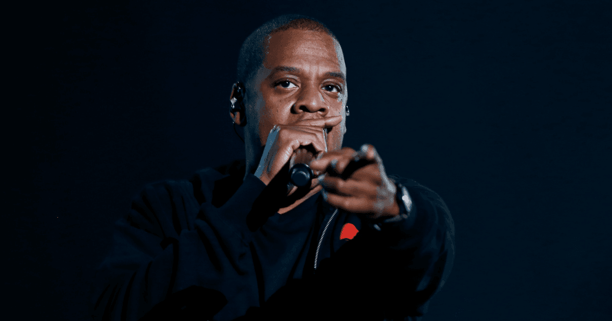 Jay-Z: A photo of the rapper Jay-Z against a black background. He is holding a microphone and rapping into it