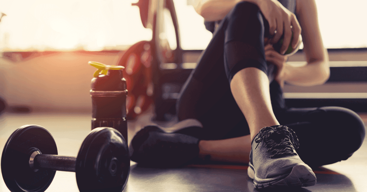 Gym: A woman sits in gym leggings on a wooden floor surrounded by weights