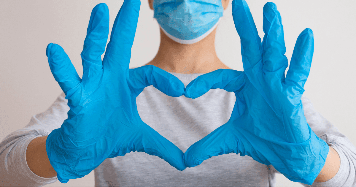 Nurses: A nurse in white overalls with blue gloves on makes a heart with their hands