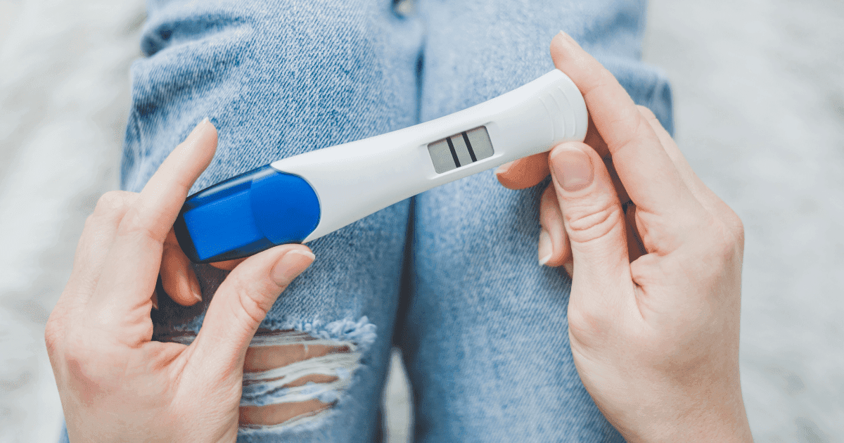 IVF: A person holding a blue and white pregnancy test looks down a positive result of two lines across a screen.