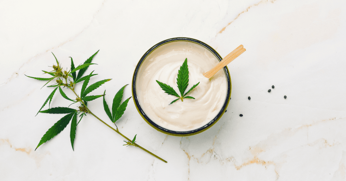 Fibromyalgia: A tub of cream with a cannabis leaf on top. There is a leaf next to the tub on a marble tabletop