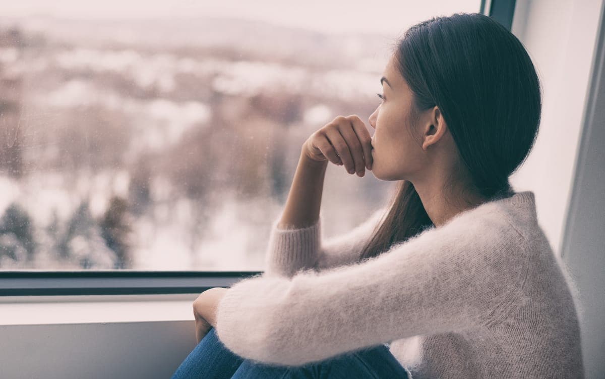 Endometriosis: woman sad comtemplative looking out the window alone.