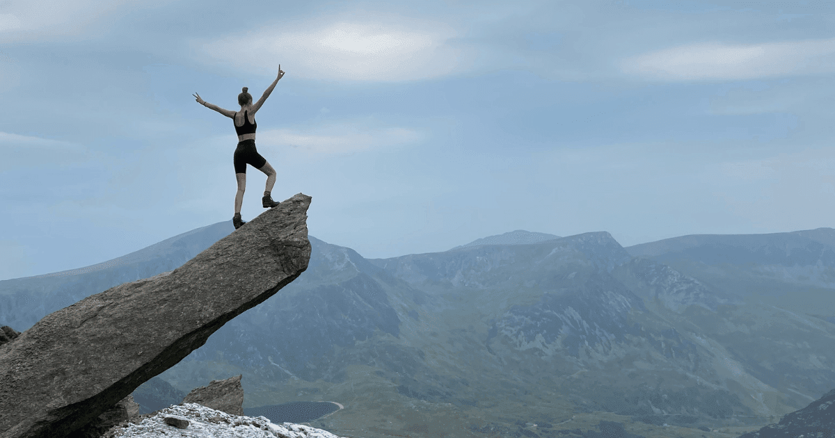 Endometriosis: A woman on top of a tall rock raising her arms in celebration of having reached the peak of the mountain