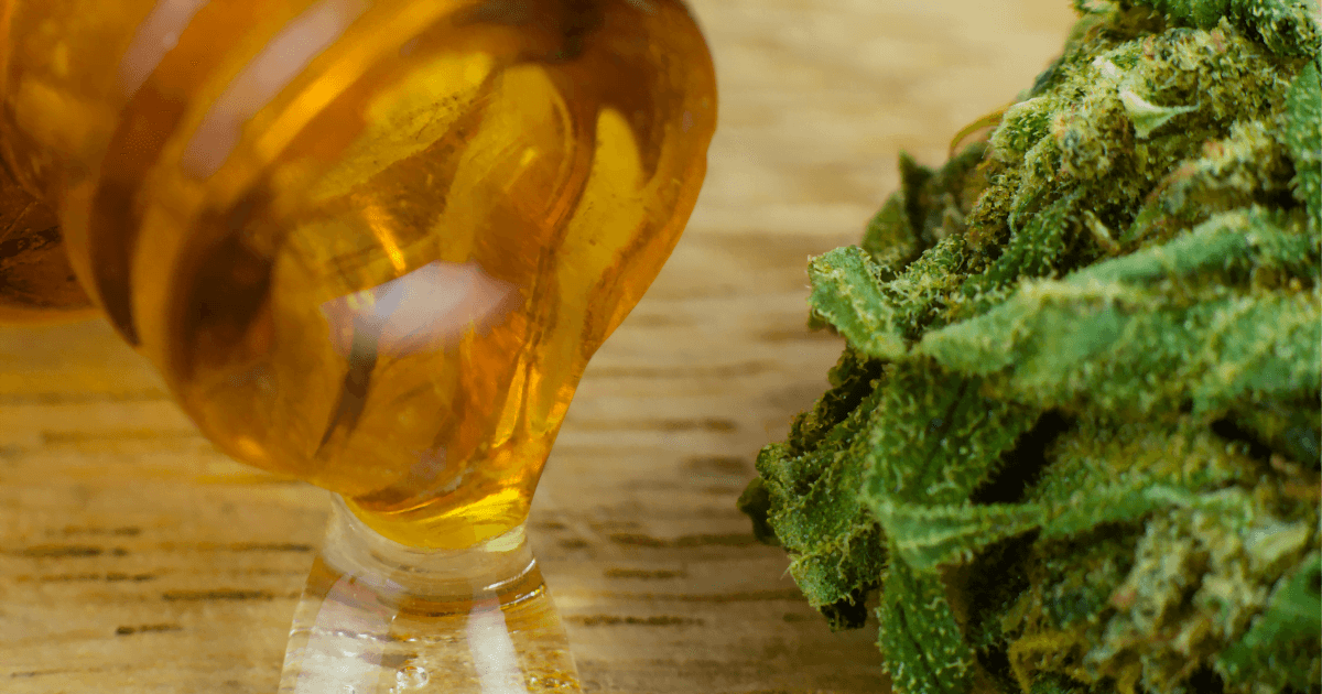 Quality of life: A bottle of CBD oil on its side pouring oil onto the wooden floor next to a cannabis bud