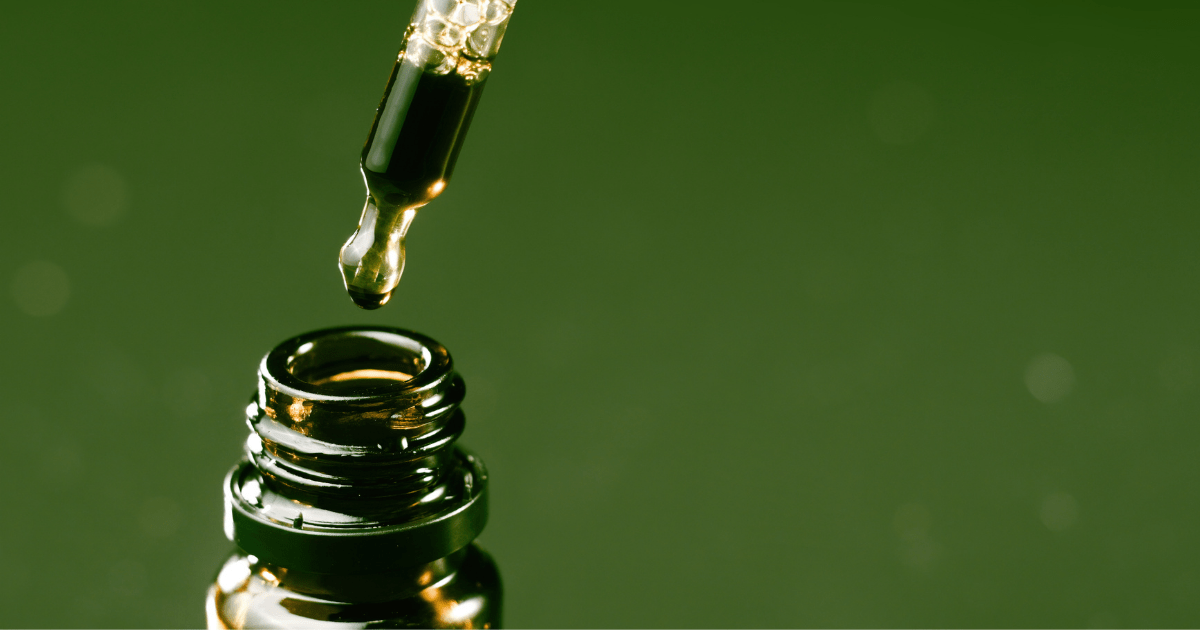Article: The top of a bottle with a dropper about to pour oil in against a green background