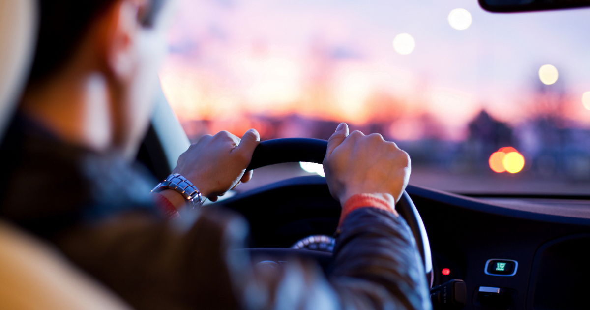 Driving and CBD: A man's hands on the steering wheel of a car against a sunset
