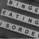 Binge eating: Scrabble tiles spelling out binge eating disorder on a wooden floor
