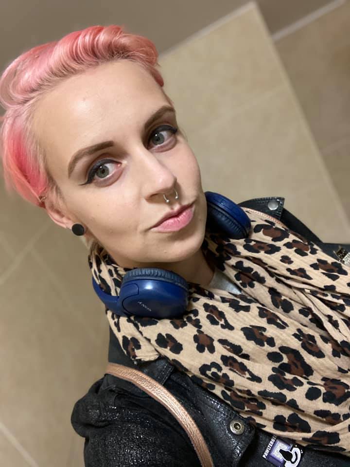 ADHD: A white woman with short pastel pink hair wears a leopard scarf and blue headphones around her neck.
