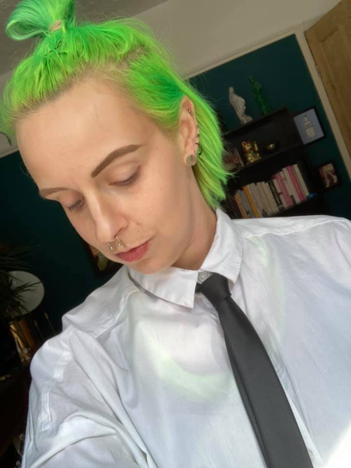 ADHD: A woman with neon green hair looks away from the camera. She is wearing a white shirt with a black tie. 