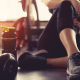 Gym: A woman sits in gym leggings on a wooden floor surrounded by weights