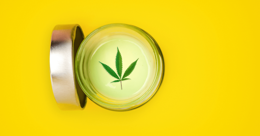 The best way to take CBD; A small jar of CBD topical gel on a yellow background. The lid off the jar and it has a cannabis leaf on the top of white cream