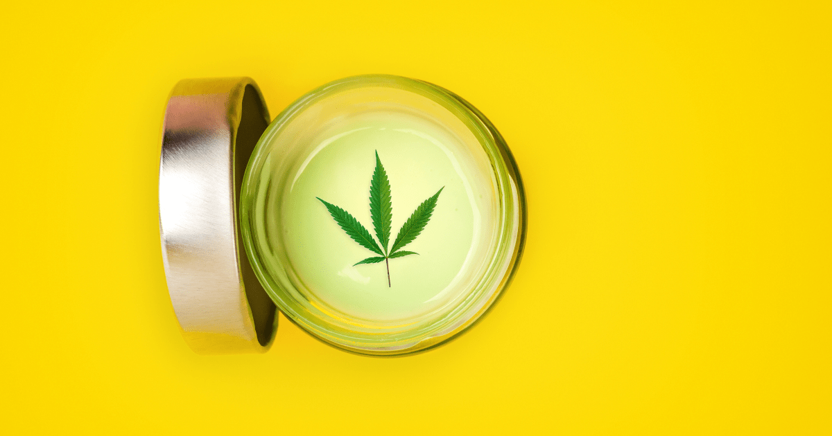 Seizures: A small jar of CBD topical gel on a yellow background. The lid off the jar and it has a cannabis leaf on the top of white cream