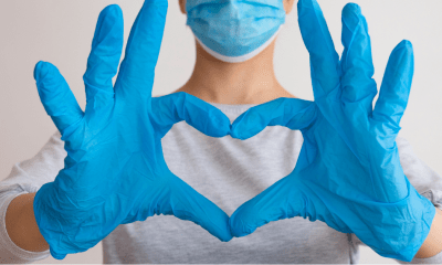 Nurses: A nurse in white overalls with blue gloves on makes a heart with their hands