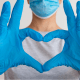 Nurses: A nurse in white overalls with blue gloves on makes a heart with their hands