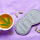 Insomnia: A sleep mask, cannabis leaves, capsules and a cup of tea with a cannabis leaf sit on a purple duvet