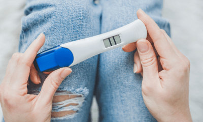 IVF: A person holding a blue and white pregnancy test looks down a positive result of two lines across a screen.