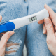 IVF: A person holding a blue and white pregnancy test looks down a positive result of two lines across a screen.