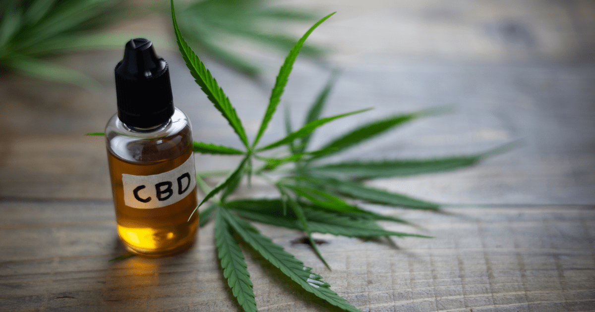 Parkinson's Disease: A bottle of yellow CBD oil sits on a wooden surface near two green cannabis leaves