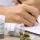 GROW: A doctor writing a medical cannabis prescription with an open canister of cannabis beside their hand