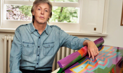 Paul McCartney: The Beatles musician wearing a denim blue shirt poses next to a multicoloured artwork
