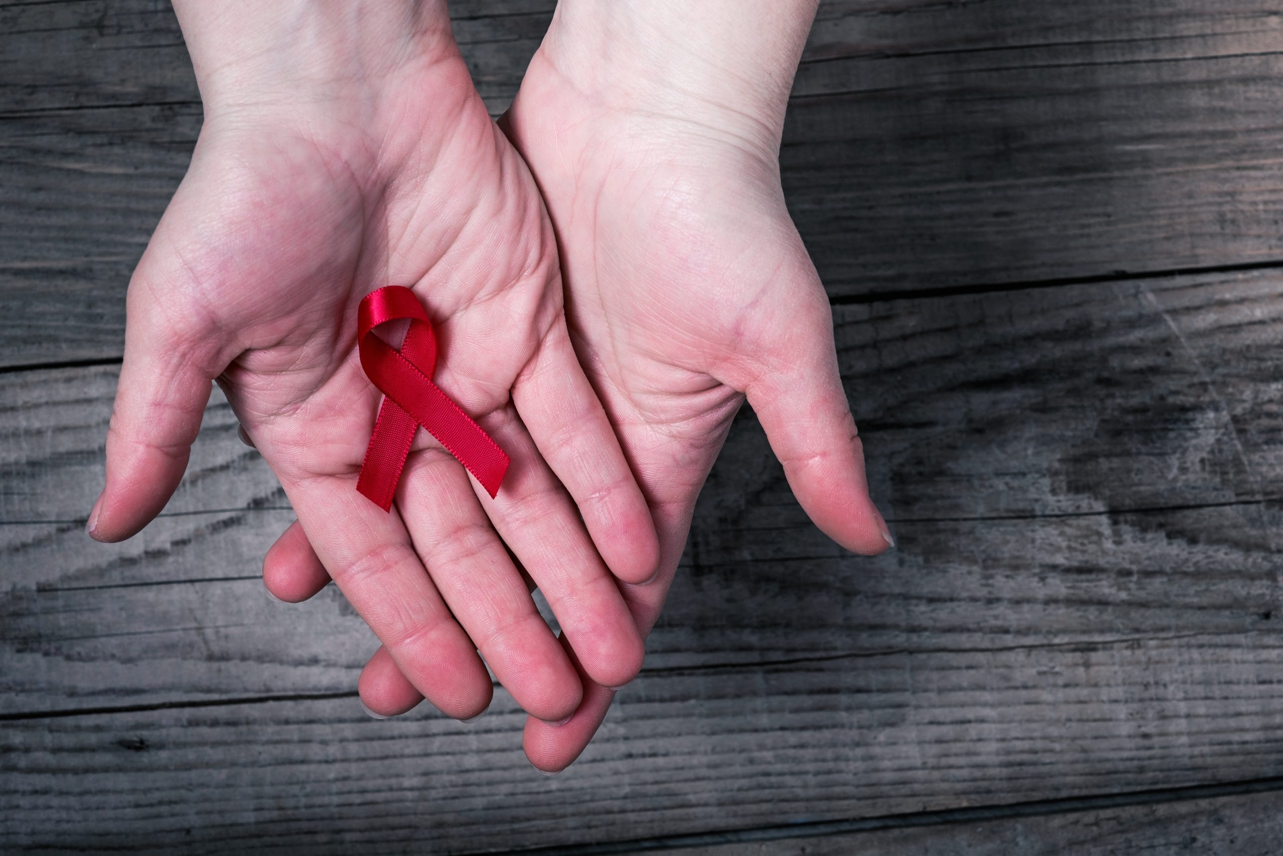 HIV: A red ribbon for World Aids Day resting in a pair of hands