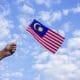 Malaysia: A malaysian flag being held up against a blue sky