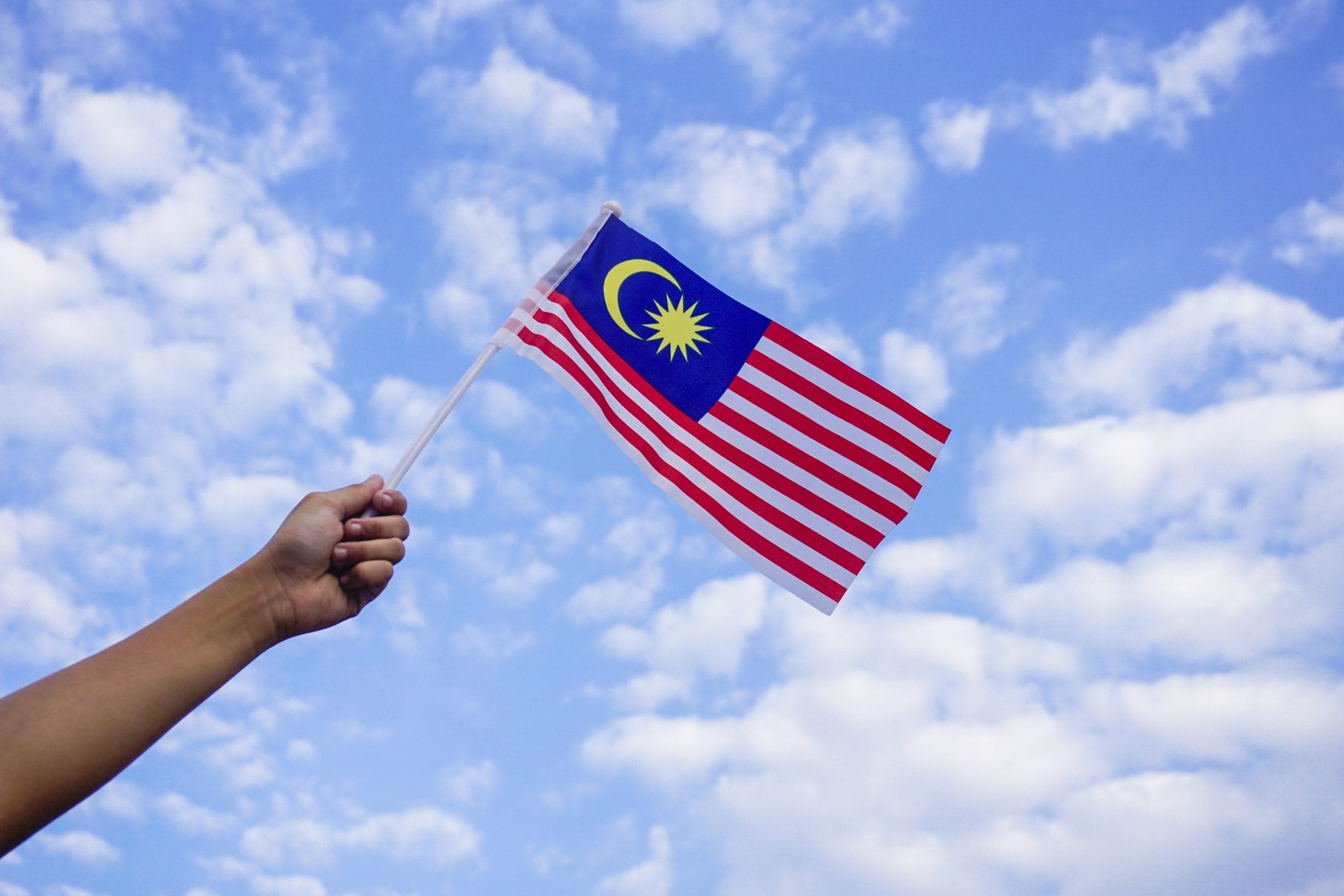 Malaysia: A malaysian flag being held up against a blue sky