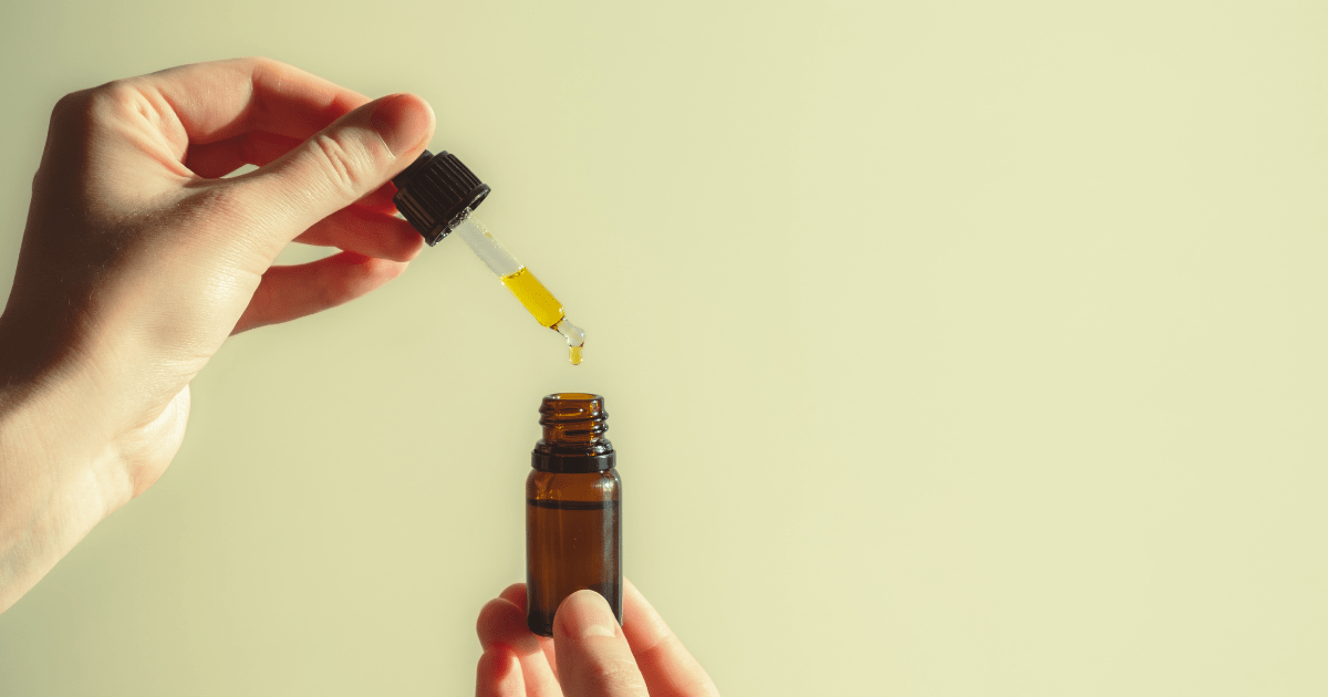 UK fibromyalgia: A hand holding a small brown bottle of CBD oil with another hand pouring oil from a dropper into it