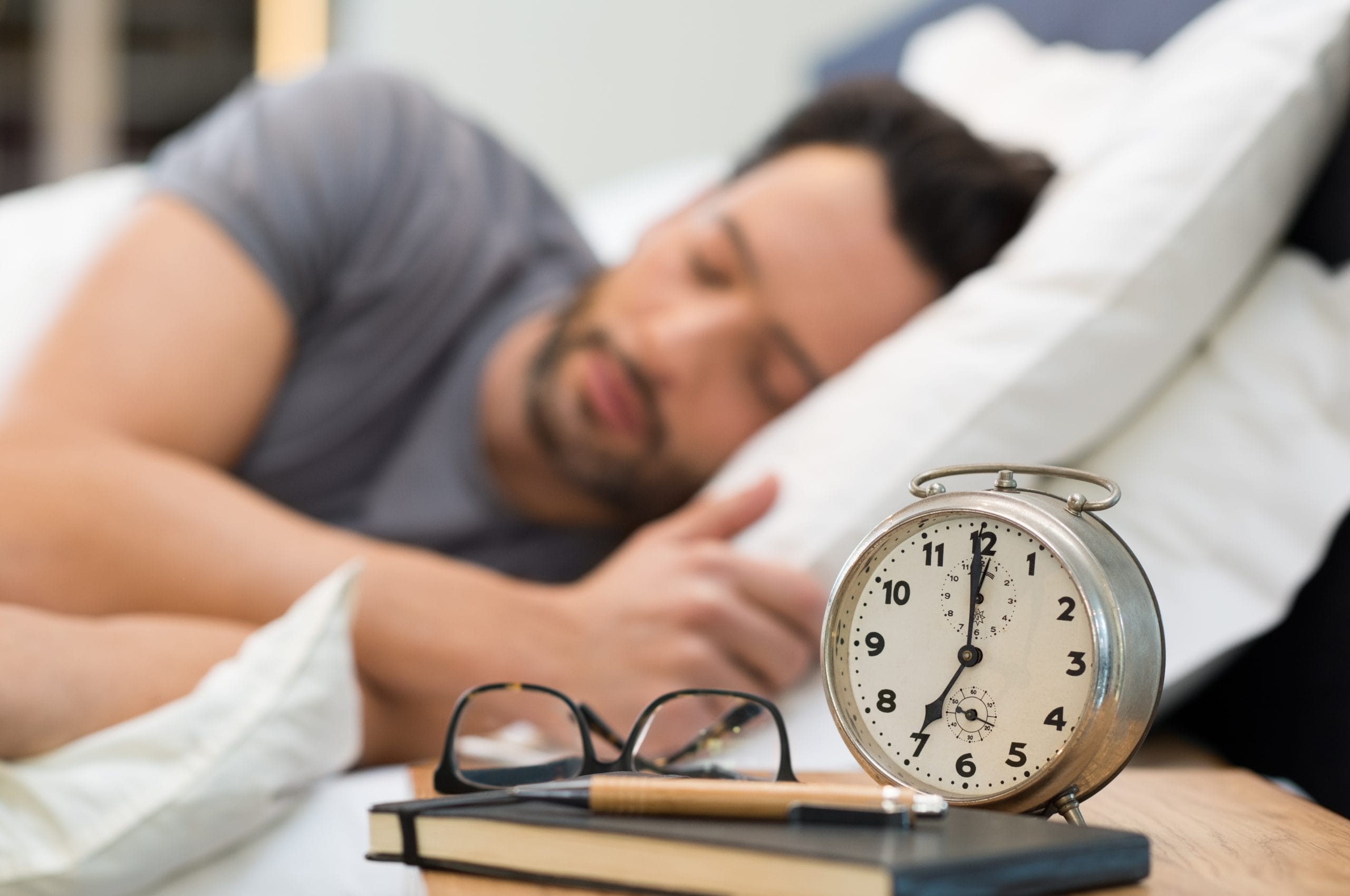 CBD: A man sleeping on a comfortable pillow with a clock in front of him on the night stand