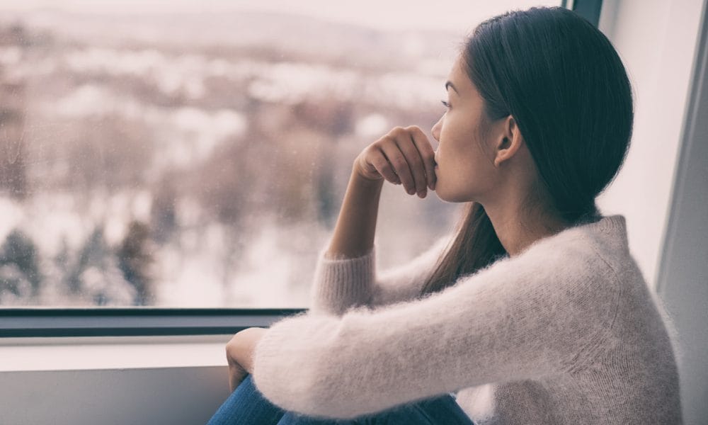 Endometriosis: woman sad comtemplative looking out the window alone.