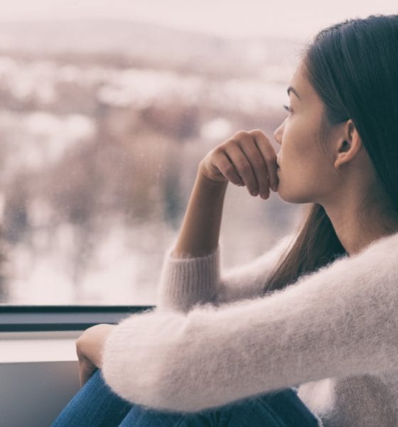 Endometriosis: woman sad comtemplative looking out the window alone.