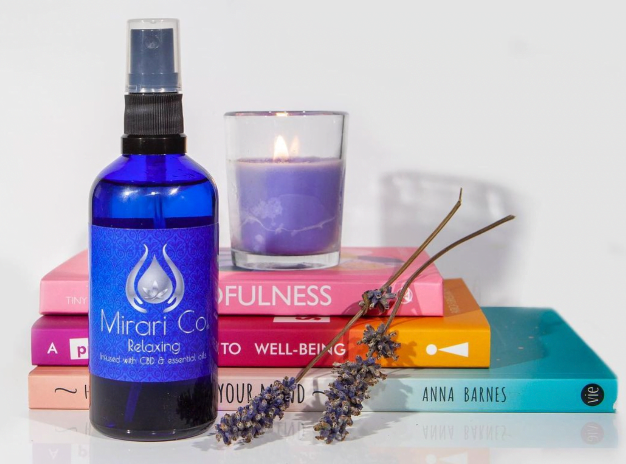 Mirari Co. A bottle of oil with candles and books on wellness