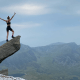 Endometriosis: A woman on top of a tall rock raising her arms in celebration of having reached the peak of the mountain