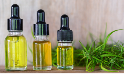 Cannabinoids: A row of three bottles of oil sitting on a shelf with a cannabis plant in the background