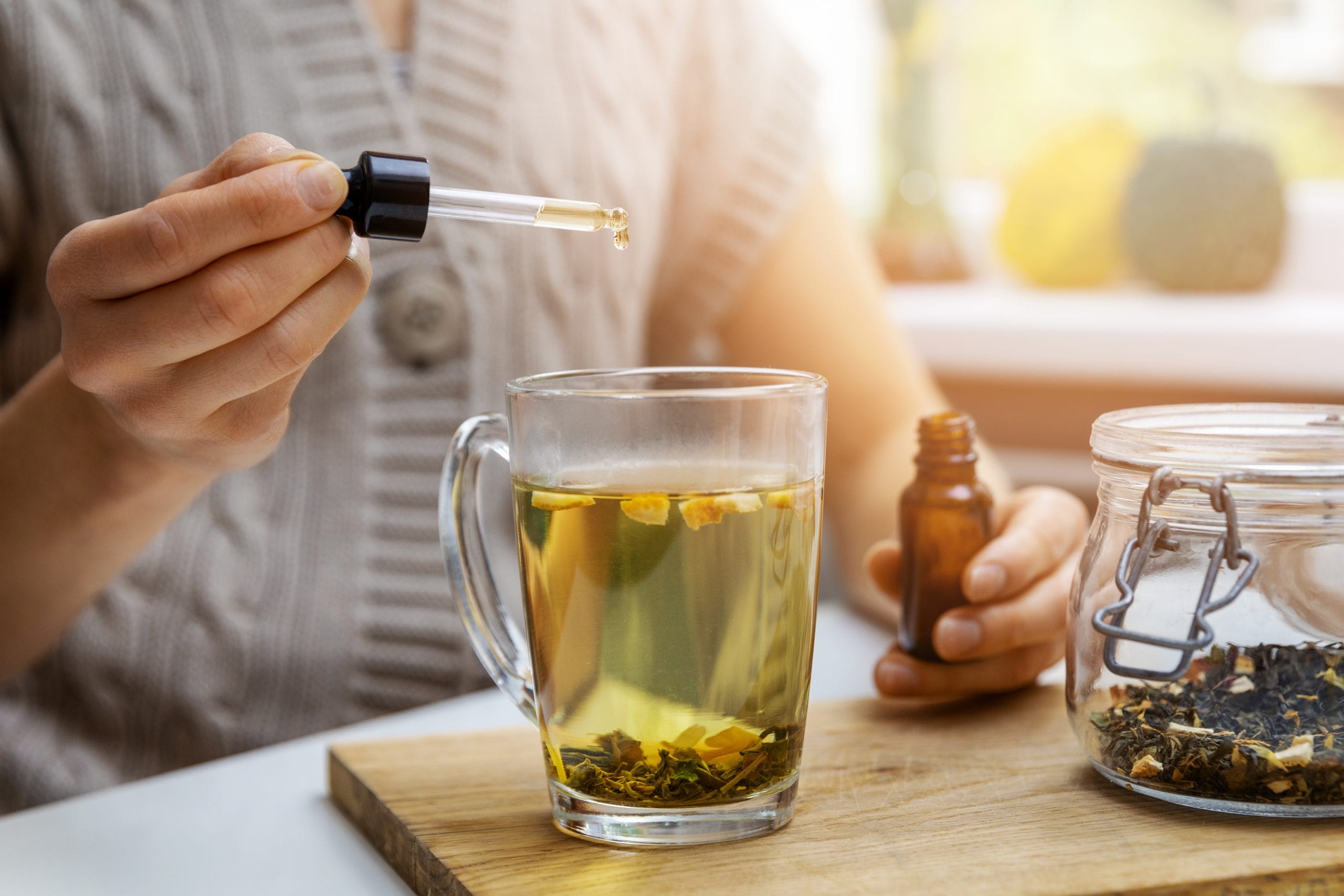 Arthritis: A person adding a drop of CBD oil to a cup of herbal tea